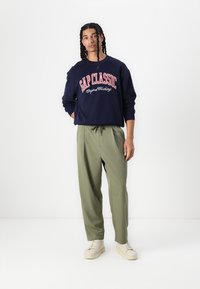 Marinblå sweatshirt med "GAP CLASSIC" i vit och röd text; olivgröna byxor; krämfärgade sneakers; avslappnad passform; mjukt tyg.