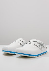 White clogs with a textured finish, featuring two adjustable silver strap buckles, and a blue accent along the sole.
