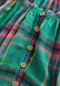 Tissu à carreaux turquoise, rose et violet avec une taille élastique froncée et cinq boutons en bois naturel alignés sur la couture centrale.