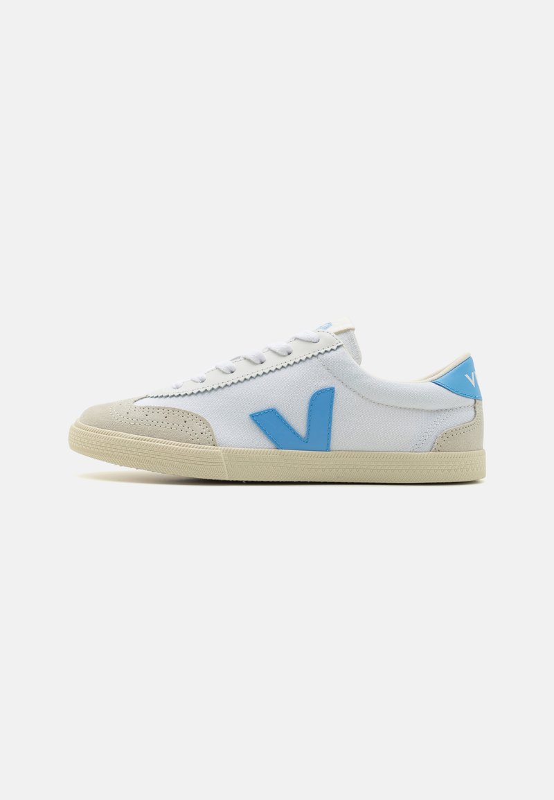 White canvas sneaker with light blue accents, beige suede toe cap, and textured rubber sole. Features a prominent blue 'V' logo on the side.