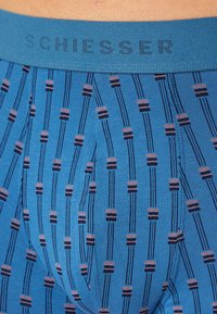 Blaue Boxershorts mit einem gemusterten Design aus vertikalen Linien und kleinen geometrischen Formen, versehen mit einem weichen blauen Bund, der mit "SCHIESSER" beschriftet ist.