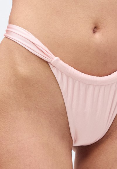 Κοντινό πλάνο του κάτω μέρους της κοιλιάς και του γοφού ενός ατόμου που φοράει ανοιχτό ροζ μαγιό μπικίνι με μαζεμένα πλαϊνά λουριά.