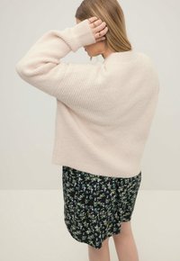 Světle růžový žebrovaný svetr spárovaný s černou sukní s květinovým potiskem, která má zelené a modré akcenty. Svetr má volný střih a spadlé ramena.