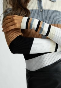 Geribbelde gebreide trui met horizontale strepen in beige, grijs, zwart en wit. Voorzien van een kraag en knopen, met gestructureerde mouwen in verschillende kleuren.