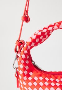 Borsa intrecciata in materiali rossi e rosa con una forma arrotondata, caratterizzata da una tracolla testurizzata, dettagli con cerniera e accenti in metallo.