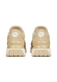 Pár béžových semišových tenisek Puma zobrazených ze zadní strany, vybavených texturovanými gumovými podrážkami a logem Puma na patních štítcích a podrážkách.