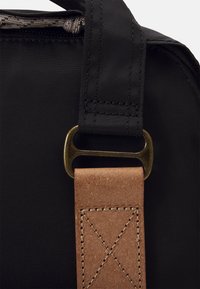 Coin de sac en tissu noir avec une sangle en cuir brun, doté d'un fermoir en métal bronze et de coutures contrastantes sur le cuir.