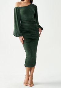 Vihreä olkaimeton, pitkähihainen mekko, jossa on rypytysdetail ja polven alapuolelle ulottuva pituus. Materiaalissa on pieni kiilto. Yhdistetty ремеtwo jalkineiden kanssa.