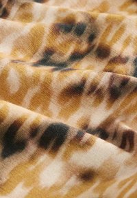Pehmeä kangas, jossa on ruskeita, mustia ja beigenvärisiä tiikeri-tyyppisiä raitoja hieman ryppyisessä kuosissa.