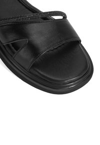 Schwarze Sandale mit einem strukturierten Lederoberteil, ausgestattet mit einem breiten Riemen und einem dünnen, verzierten Riemen über dem Fuß. Abgerundete Zehenform.