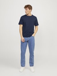 T-shirt bleu marine à col rond associé à un jean en denim bleu clair et des baskets blanches. Le mannequin se tient avec les mains dans les poches, tourné légèrement vers la gauche.