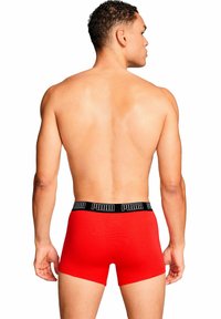 Pantaloni boxer rossi in cotone elastico, con fascia nera in vita recante il logo "PUMA". Design a gamba corta e vestibilità aderente.