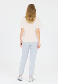 Lichtbeige T-shirt met korte mouwen, gecombineerd met grijze joggingbroek met ribbels aan de mouwen en een gestructureerde stof. Model toont de achteraanzicht. Zilveren sneakers.