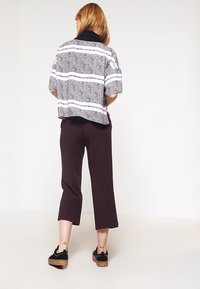 Avskuren, kortärmad topp med svart och vit randig mönster; tillsammans med mörka byxor och svarta skor med en strukturerad sula.