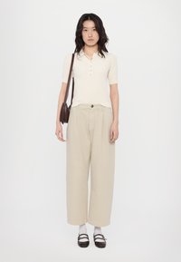 Light beige short-sleeve polo shirt with buttons, paired with wide-leg beige trousers. Black shoes and white socks complete the outfit.