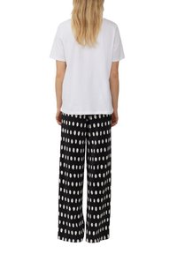 T-shirt blanc en coton associé à un pantalon large noir avec un motif de points blancs. La tenue a une coupe décontractée et informelle.
