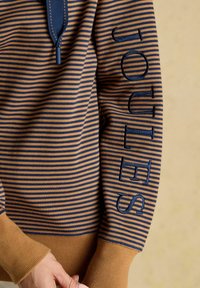 Pruun ja tumesinine triibuline svettshirt, millel on ribakäised ja "JOULES" tikand sobivas sinises niidis varruka ääres.