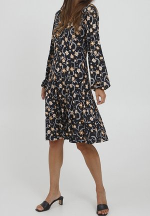 Schwarz mit floralem Muster, langärmliges Kleid mit ausgestellt Rock und entspannter Passform. Akzentuiert mit beigen und weißen Blumen, weicher Stofftextur.