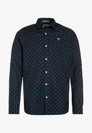 Marineblauses Hemd mit langen Ärmeln, grünen Punkten, einem Button-Down Kragen und weißen Knöpfen. Mit einem kleinen Logo auf der Brust.