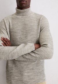 Hellgrauer, gerippter Rollkragenpullover mit taillierter Passform und langen Ärmeln. Der Stoff hat eine strukturierte Optik mit subtilen Tonvariationen.