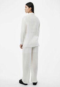 Conjunto de tejido blanco, ligero y texturizado que incluye una blusa de manga larga y pantalones holgados, combinado con sandalias de plataforma negras.