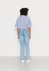 Camisa corta de rayas azules y blancas con mangas cortas, combinada con jeans ajustados de color azul claro. Calzado blanco visible. Diseño sencillo, estilo casual.