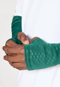 Roheline käsiülik, mis on valmistatud tekstureeritud, hingavast kangast ja millel on sõrmeaukude disain, kantud valge särgi peal, näidates detailseid mustreid.