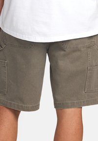 Pantaloni scurți cargo în verde măsliniu, realizați dintr-un material durabil. Prezintă două buzunare laterale mari, detalii cusute și un tiv drept.
