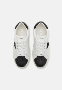 White and black leather sneakers with a smooth finish, featuring a white lace-up front, logo on the tongue, and contrasting textured panels.