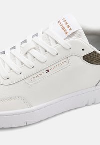 Sneaker en cuir blanc avec des panneaux en mesh, logo en relief et lacets blancs. Présente une semelle texturée et des coutures contrastées. Conception durable.