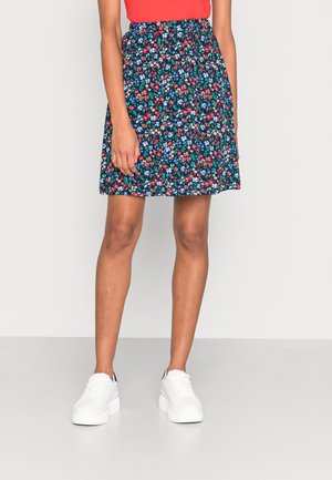 Woman wearing a knee-length navy skirt with red, blue, and white floral print, paired with white sneakers and a red top.