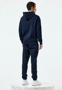 Marineblaues Kapuzenpullover mit Kordelzugkapuze, kombiniert mit passenden Jogginghosen. Verfügt über gerippte Bündchen und Saum, getragen mit weißen Sneakers.