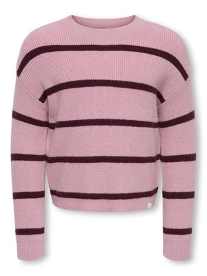 Child with curly hair wearing a pink striped sweater, wide-leg black pants, and pink shoes, standing with hands in pockets and smiling.