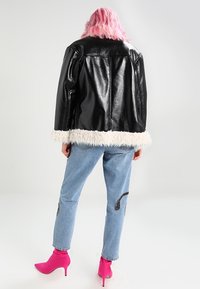 Svart läderjacka med faux fur-fåll, tillsammans med ljusblå jeans med dekorativ sömnad. Modellen bär klarröda ankelskor.