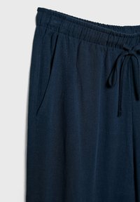 Granatowe spodnie wykonane z miękkiego, strukturalnego materiału, z elastycznym paskiem, zapięciem na sznurki i bocznymi kieszeniami.