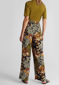 Haut vert à manches courtes associé à un pantalon à jambes larges avec un motif floral et de feuilles multicolore, taille élastique, et sandales.
