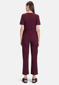 Bordeaux jumpsuit met korte mouwen, elastische tailleband en wijde pijpen. Gemaakt van zachte stof, het heeft een eenvoudige ronde halslijn.