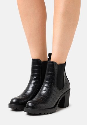 Bottines noires à texture crocodile, avec des panneaux élastiques sur les côtés, un bout carré et un talon épais. Semelle robuste pour une meilleure adhérence.
