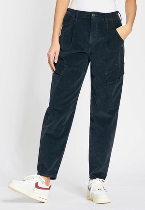 Dunkelblaue Corduroy-Cargo-Hosen mit hohem Bund, vorderen Falten, Seitentaschen und schmal zulaufenden Beinen, kombiniert mit weißen Sneakers mit roten Akzenten.