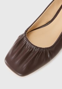 Brown leather flat shoe with a rounded square toe, elasticated collar, and smooth finish. Textured upper with a relaxed fit design.