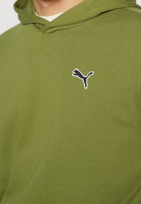 Olivově zelená mikina s texturovanou tkaninou. Na levé části hrudi je vyšitý černý logo Puma. Obsahuje kapuci a žebrované manžety.