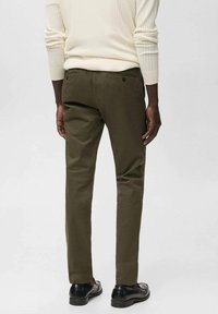 Olive green slim-fit trousers with a smooth texture, two back pockets, and subtle stitching details, paired with black shoes.