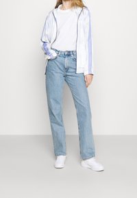 Bílá a světle fialová zipová bunda, bílá tričko, světle modré volné džíny a bílé tenisky. Klasický sportovní outfit s síťovanou texturou.