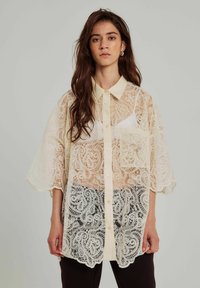Blusa in crema con sovrapposizione di pizzo, colletto, maniche corte, chiusura a bottoni e intricati motivi paisley sull'orlo.
