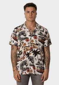 Camisa de manga corta, con botones, hecha de una tela ligera que presenta un colorido patrón tropical con olas, flores y tablas de surf. Acentos en blanco y negro.