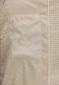 Beige stoffen interieur toont een gestikte zak met een witte hand- en harticoon en cirkelvormige tekst over zorglabels erin.