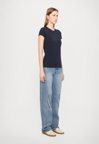 T-shirt in cotone blu navy con maniche corte e un logo discreto sulla parte anteriore, abbinata a jeans larghi di colore blu chiaro con un motivo stampato.