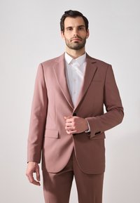 Helles rosa Sakk mit Schalkragen, Ein-Knopf-Verschluss und zwei vorderen Taschen, kombiniert mit einem weißen Hemd.