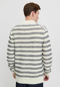 Pulover tricotat ușor, de culoare crem, cu dungi bleumarin; are un guler rotund, mâneci lungi și manșete și tiv ribbate. Model texturat pe întreaga suprafață.