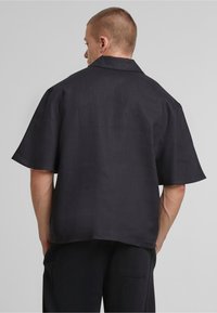 Black short-sleeve shirt with a relaxed fit, featuring a collar, subtle texture, and plain design, shown from the back.